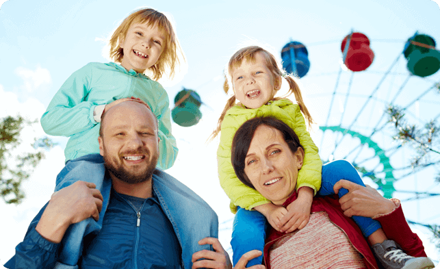 A family is holding their children in front of a ferris wheel.