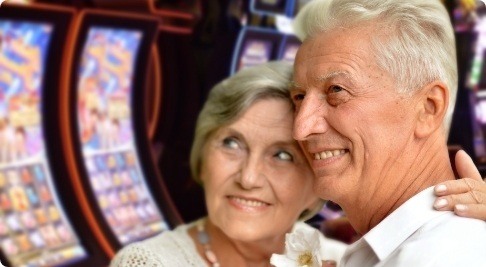 An older couple posing in front of slot machines.