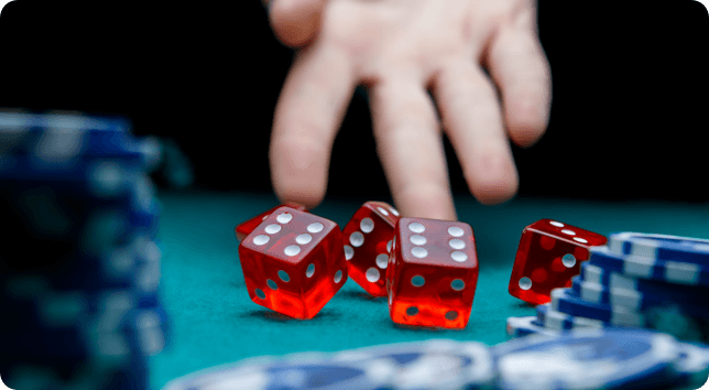 A hand with red dice and chips on a table.