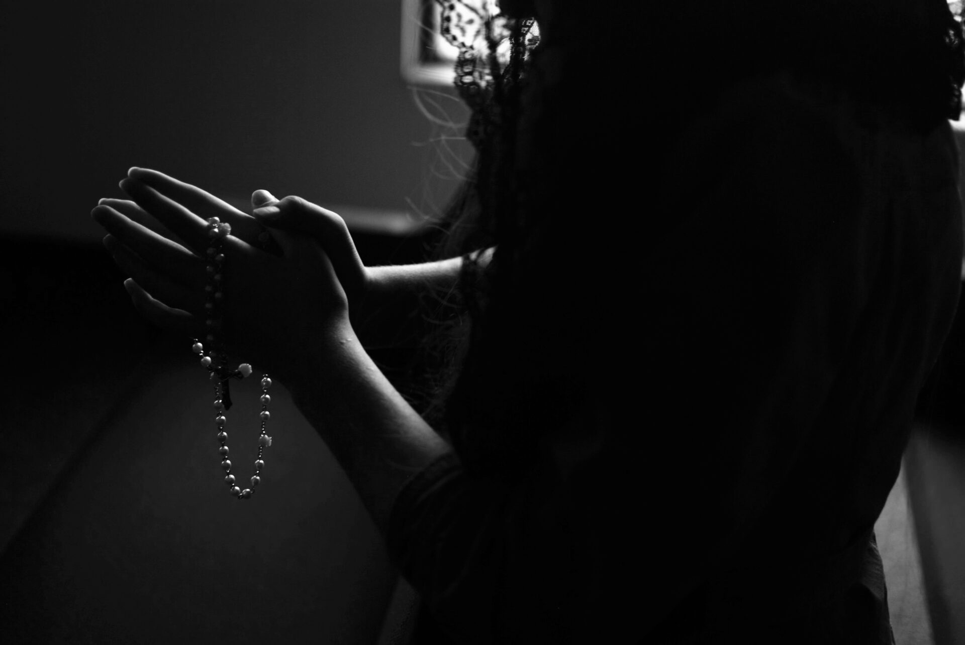 A black and white photo of a woman praying with a rosary.