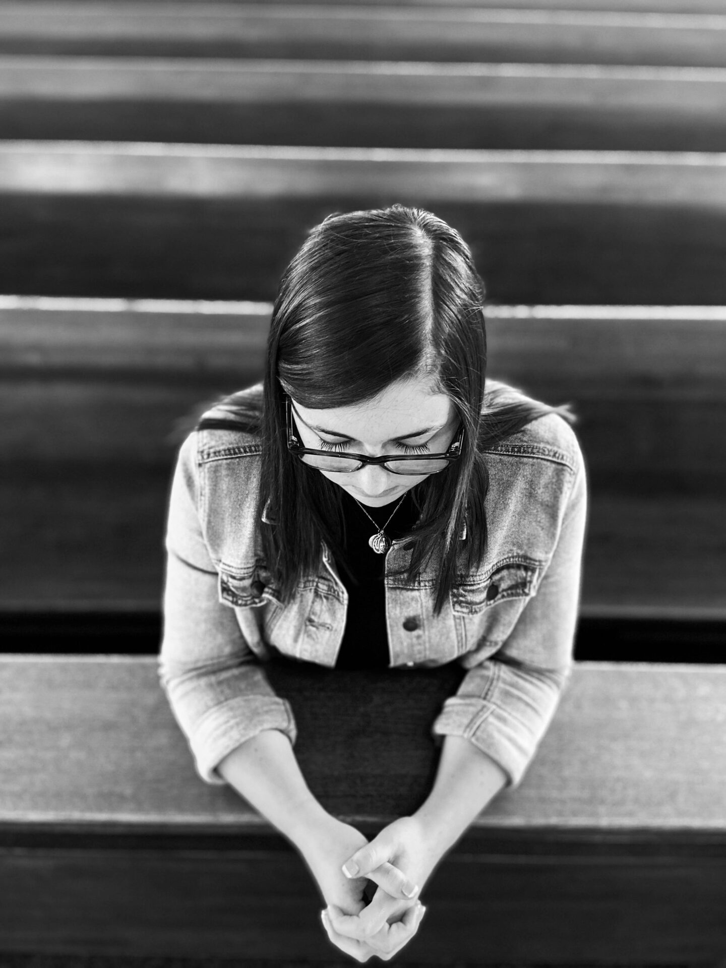 A black and white photo of a woman praying in a church pew.