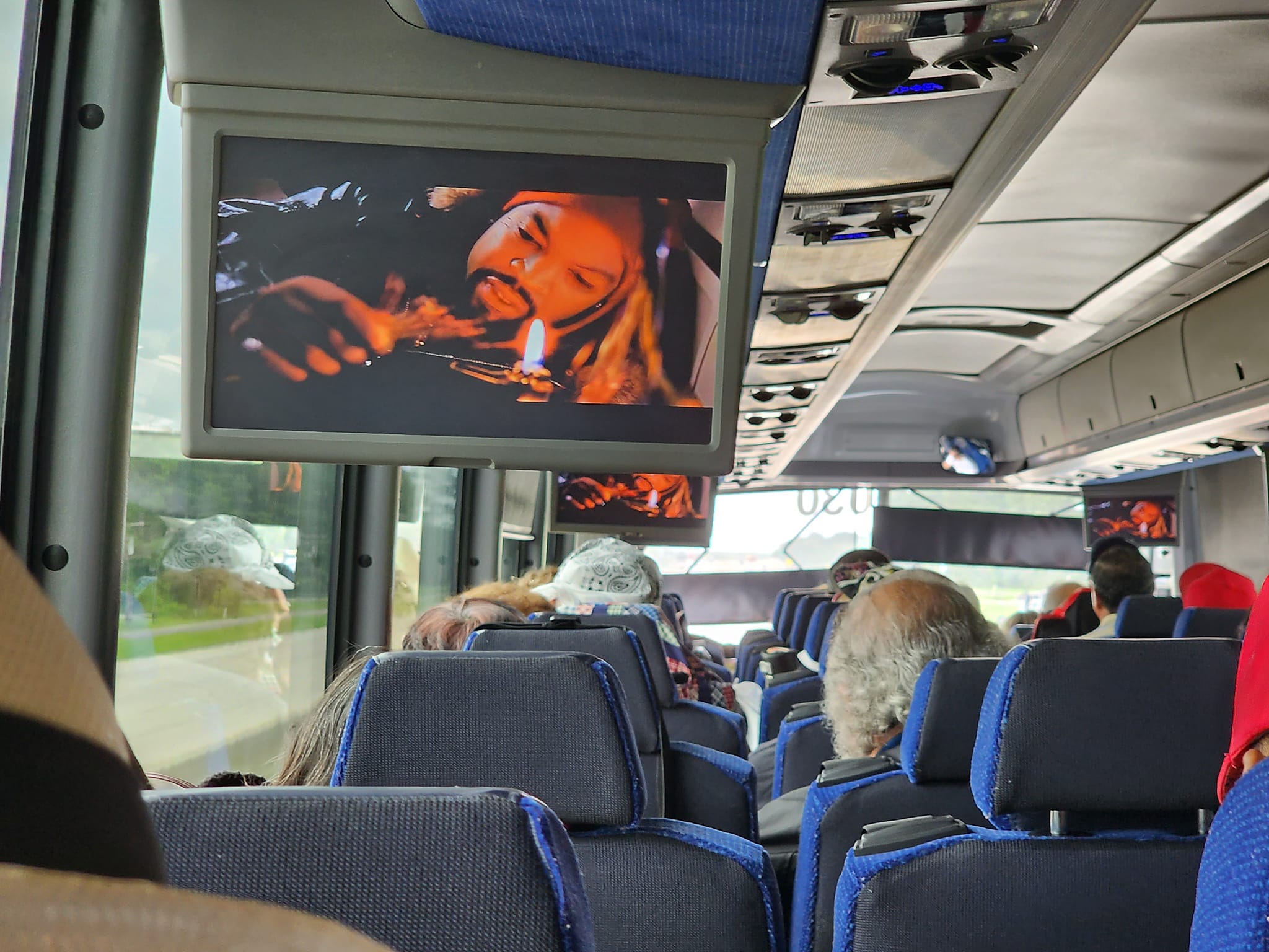 A group of people on a bus watching tv.